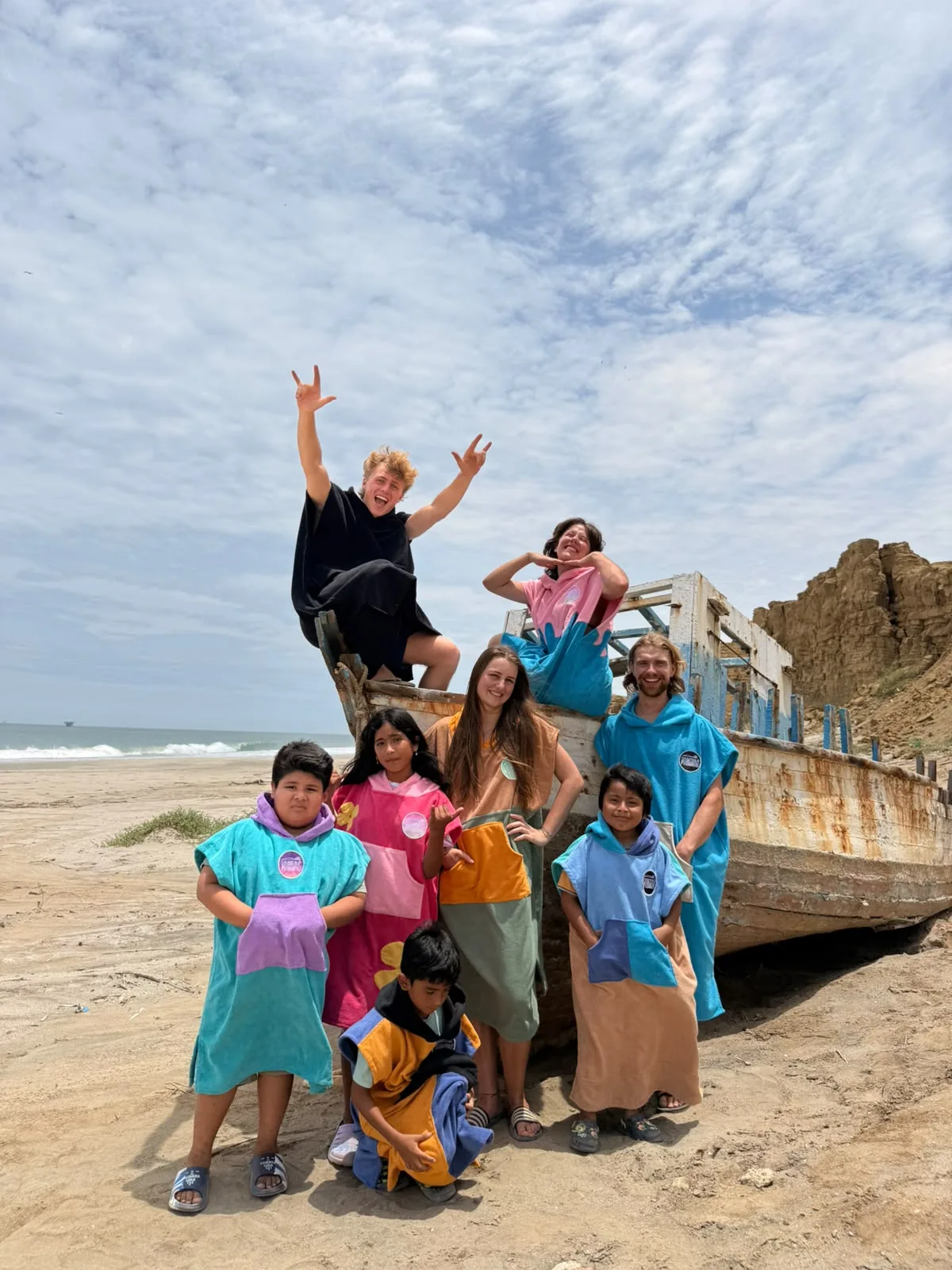 Niños del pueblo y visitantes con ponchos sobre un bote de pesca en la playa de Lobitos